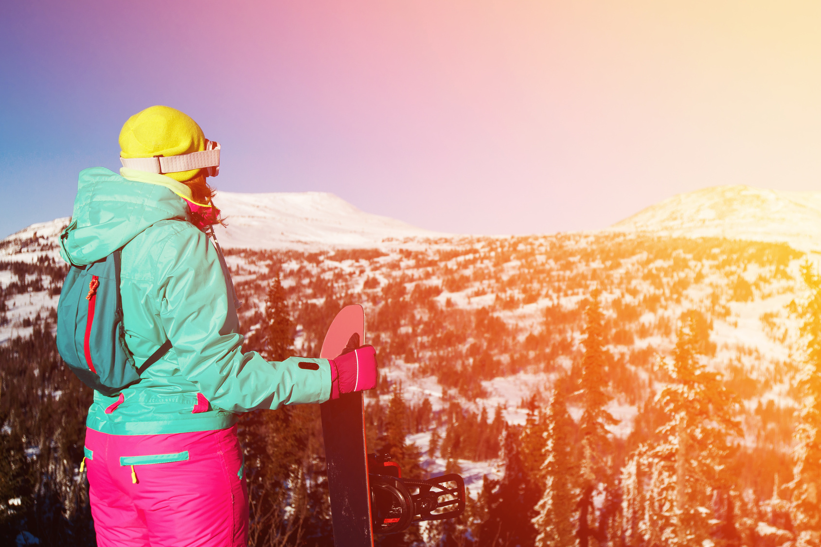 Girl is holding a snowboard and looking at the mountains and forest. Freeride snowboarding in Sheregesh Ski Resort